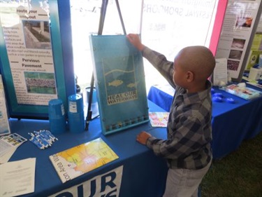 A child plays Heal Our Waterways Plinko at Earth Day festival.