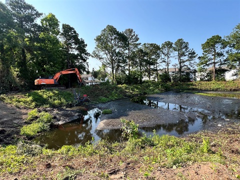 View of a wet pond with an excavator driving around it.