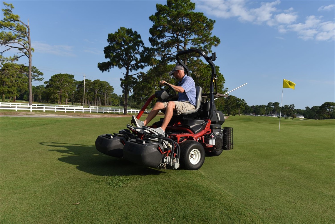 A man riding a lawnmower at the Municipal Golf Course.